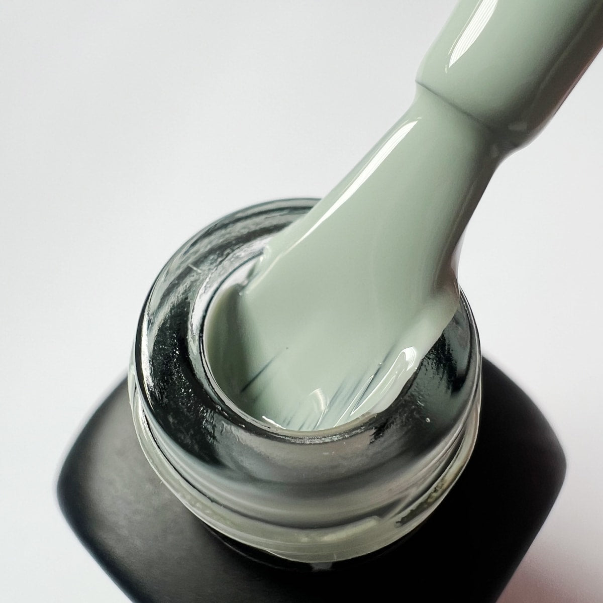 Pennello dello smalto verde salvia Matcha estratto dal collo del flacone, che mostra la consistenza del colore.