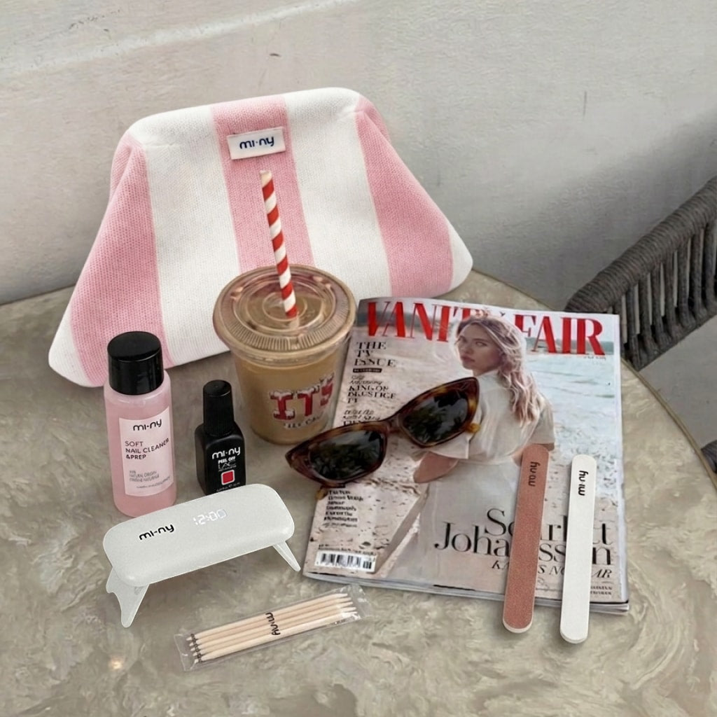 Kit unghie MI-NY con beauty case a righe rosa, smalto Peel Off, lampada led, lime e bastoncini, disposti su un tavolino con rivista Vanity Fair e occhiali da sole